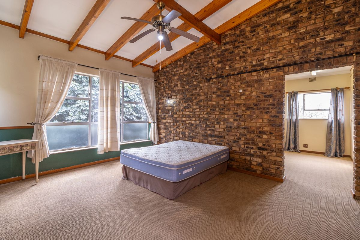 Spacious bedroom featuring exposed timber ceiling beams, a rustic brick feature wall, and large windows allowing for ample natural light.