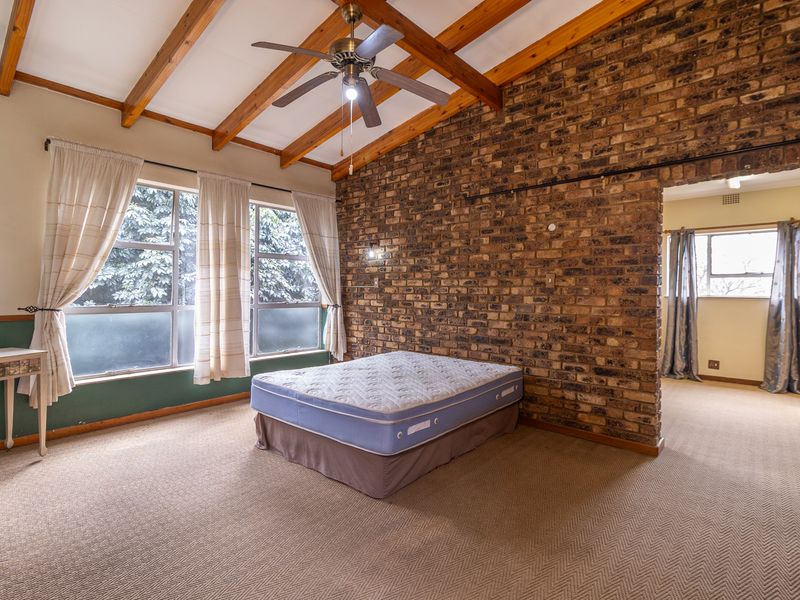 Spacious bedroom featuring exposed timber ceiling beams, a rustic brick feature wall, and large windows allowing for ample natural light.