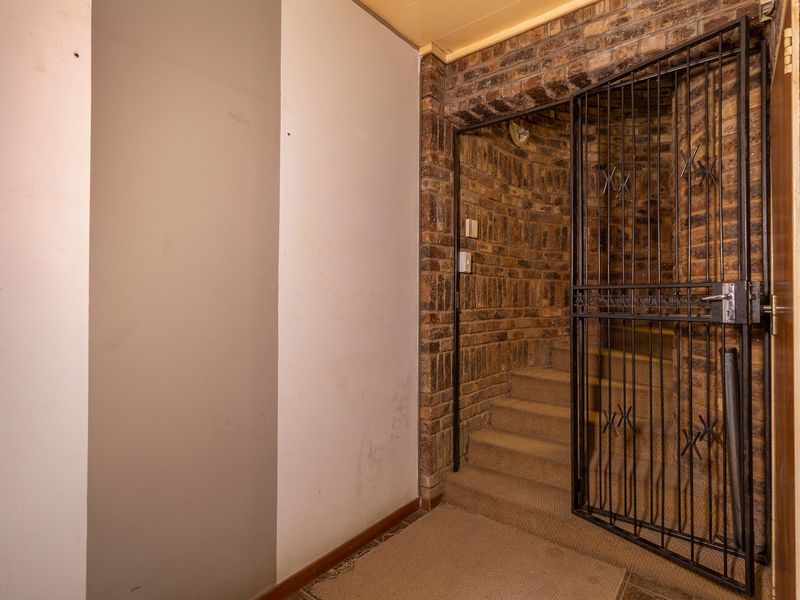 A hallway area featuring exposed brick walls, a security gate, and a carpeted staircase leading to another level.