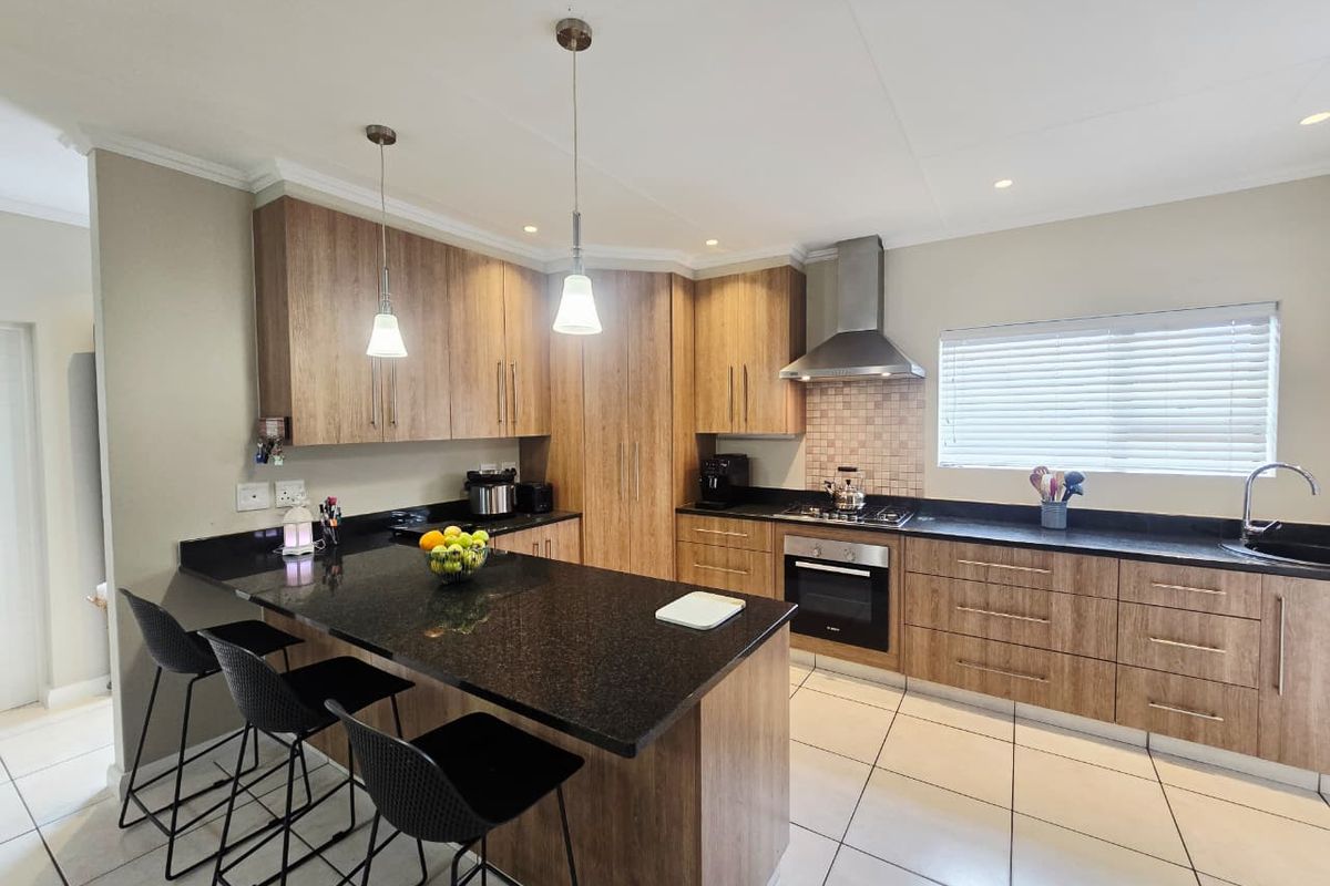 Modern kitchen featuring wood-look cabinetry, granite countertops, a central island, and integrated stainless steel appliances with tiled flooring.