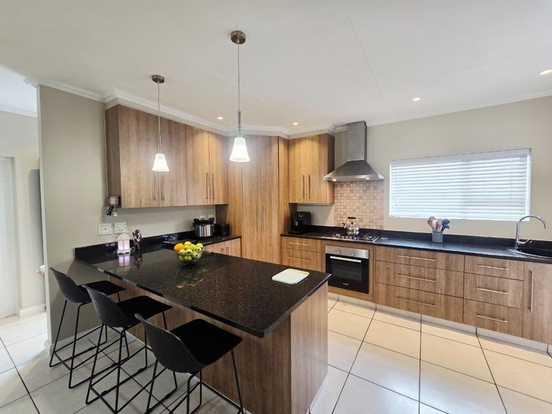 Modern kitchen featuring wood-look cabinetry, granite countertops, a central island, and integrated stainless steel appliances with tiled flooring.