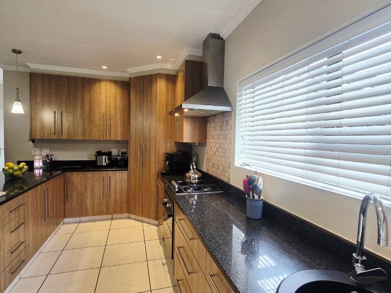 Modern kitchen featuring wooden cabinetry, granite countertops, stainless steel extractor fan, gas hob, and tiled flooring with a functional layout.
