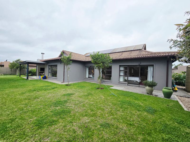 Rear view of the house featuring a landscaped garden, covered patio with built-in braai, sliding glass doors, and roof-mounted solar panels.