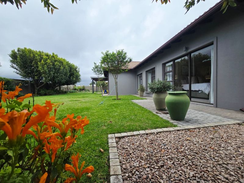 A well-maintained rear garden featuring a paved patio area, manicured lawn, and sliding glass doors providing access to the interior living space.