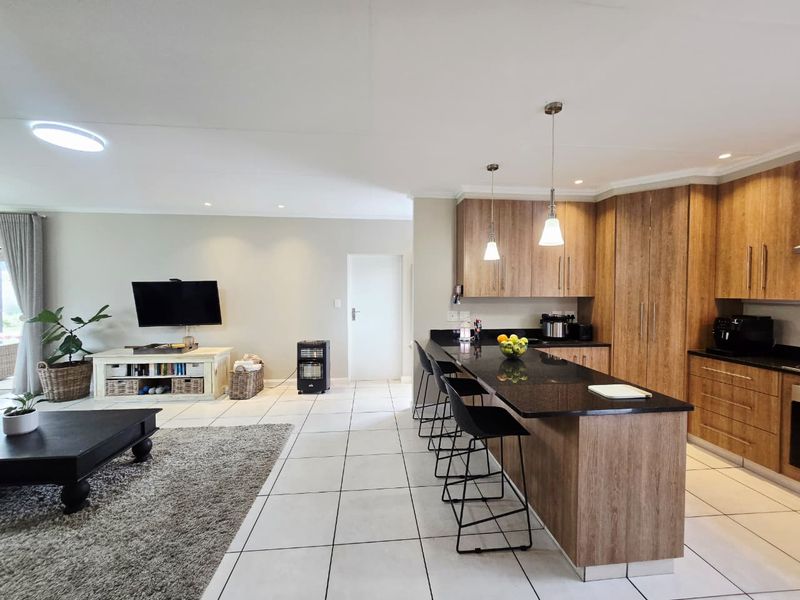 Spacious open-plan living area featuring a modern kitchen with wood-finish cabinetry, granite countertops, a central island, and tiled flooring throughout.