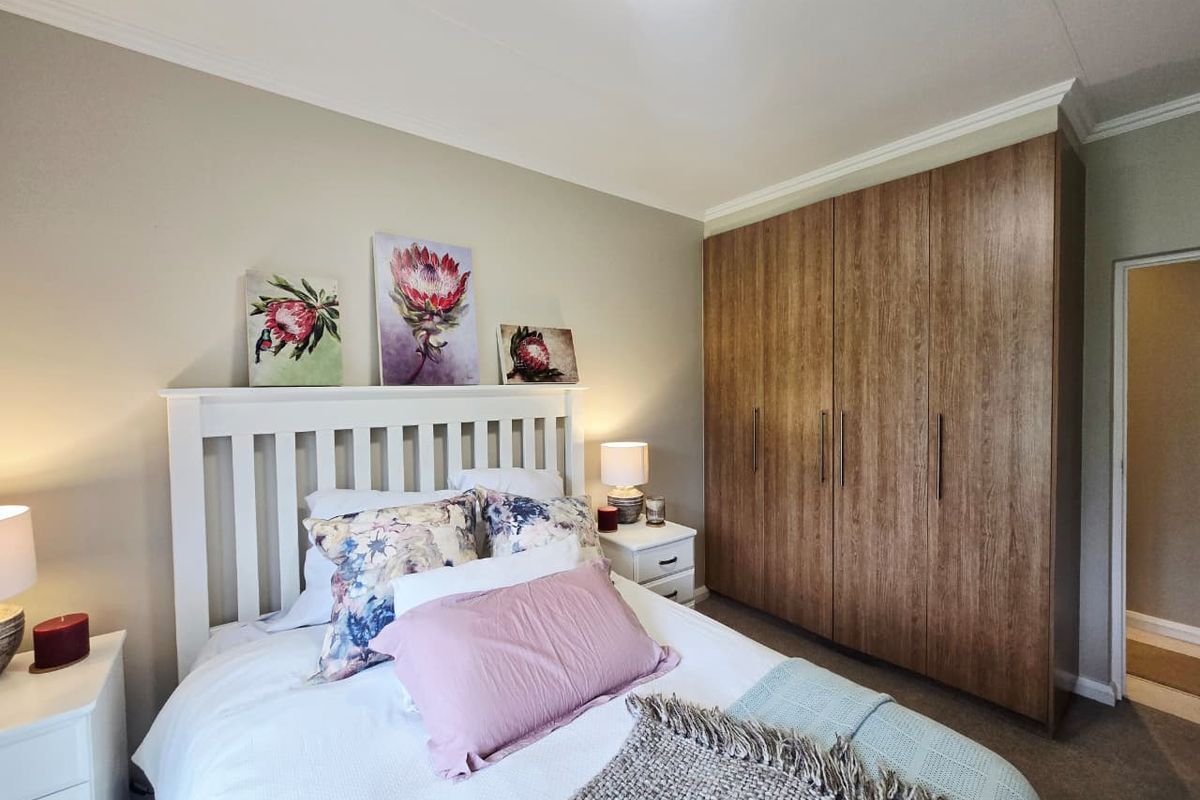 A well-maintained bedroom featuring a large, modern wood-finish built-in wardrobe, neutral wall tones, and classic cove cornice detailing.