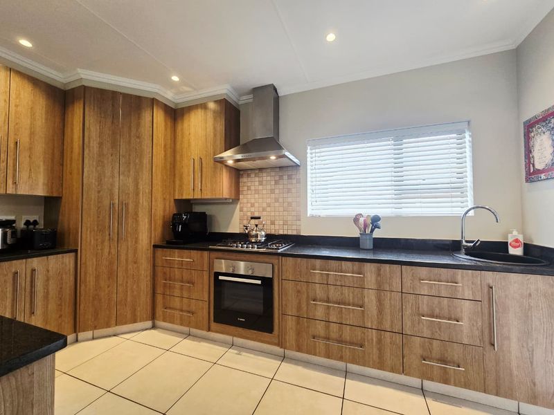 Modern kitchen featuring wood-look cabinetry, black granite countertops, built-in oven, gas hob, and stainless steel extractor fan with tiled flooring.