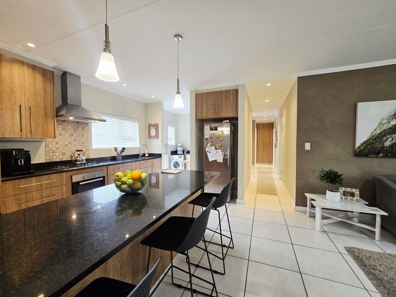 Modern open-plan kitchen featuring granite countertops, built-in appliances, and tiled flooring, seamlessly flowing into the living area and hallway.