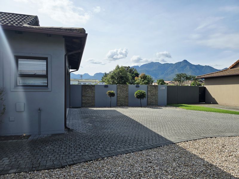 A well-maintained front exterior featuring a paved driveway, stone-accented boundary wall, and scenic mountain views.