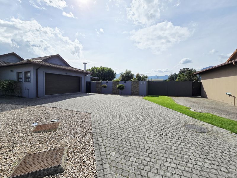 Front exterior view of the property featuring a paved driveway, double garage, and modern boundary wall with stone cladding accents.