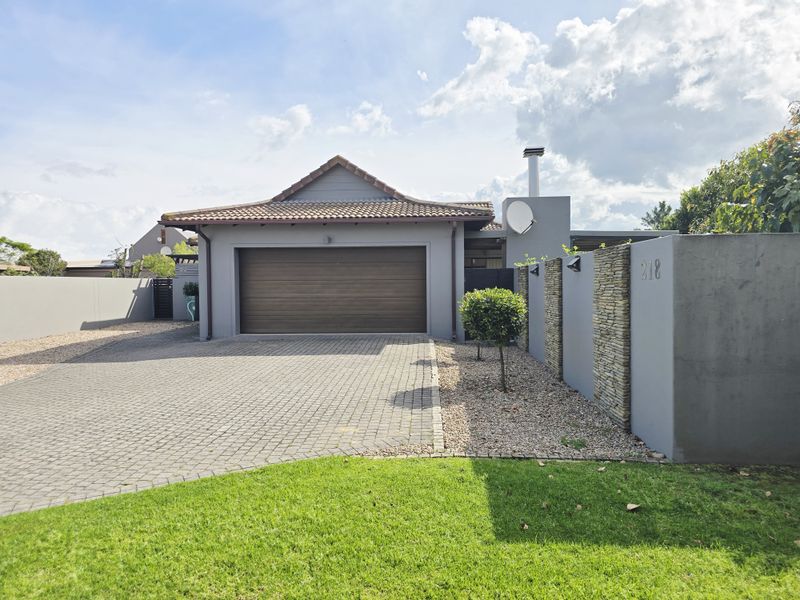 Modern front elevation featuring a paved driveway, sectional garage door, and attractive stone-clad boundary wall with well-maintained landscaping.