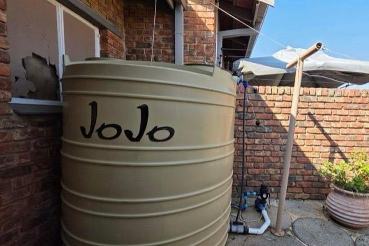 Rear exterior area featuring a large water storage tank with an integrated pump system against a brick wall.