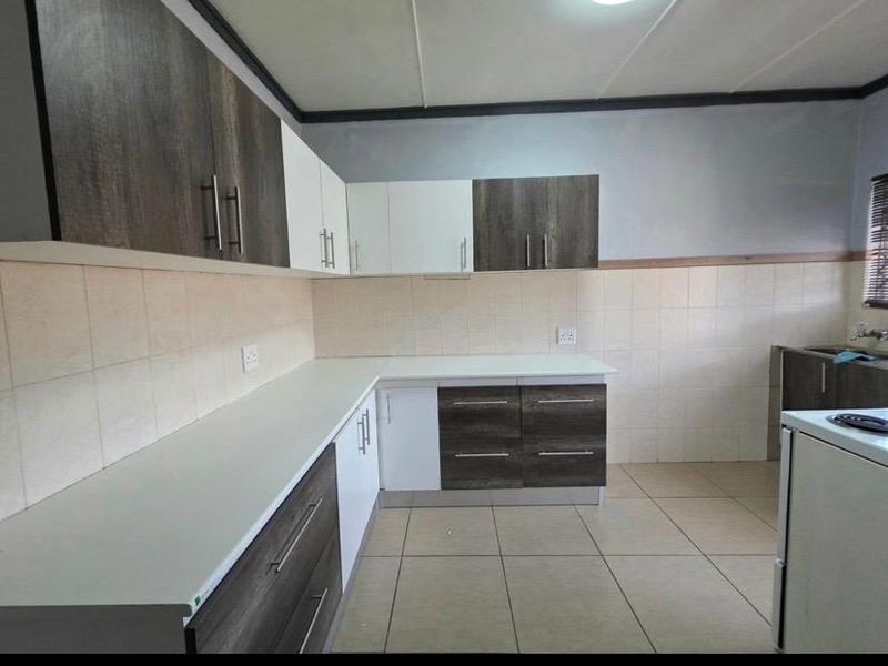 A clean, functional kitchen featuring modern two-tone cabinetry, ample counter space, tiled backsplash, and neutral floor tiles.