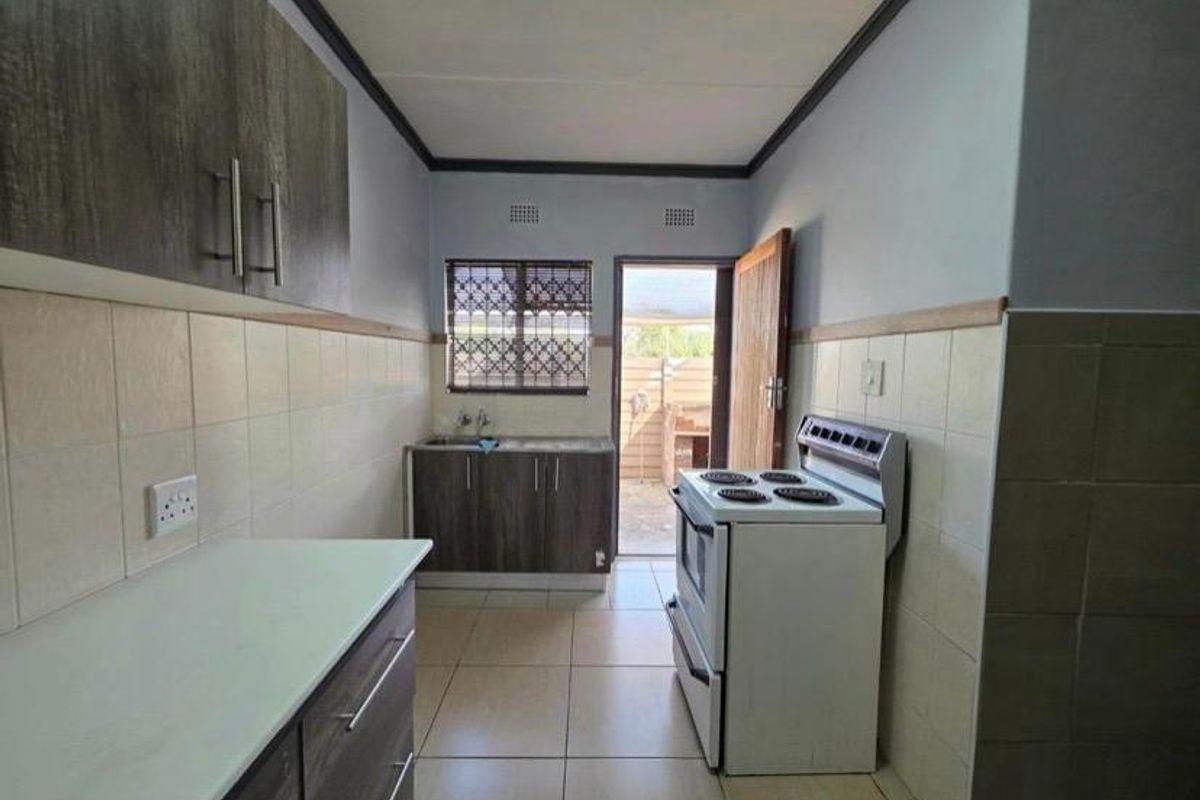 A functional kitchen featuring built-in cabinetry, tiled splashbacks, and a freestanding stove, with direct access to an outdoor area.