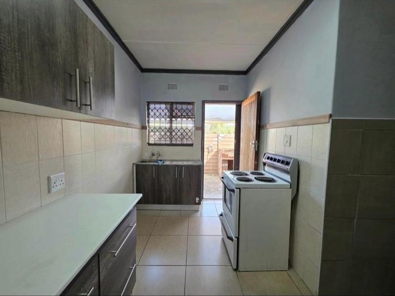 A functional kitchen featuring built-in cabinetry, tiled splashbacks, and a freestanding stove, with direct access to an outdoor area.