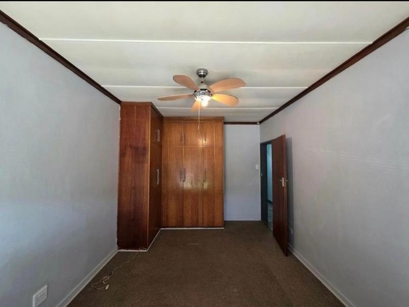 A bedroom featuring built-in wooden cupboards, a ceiling fan, and carpeted flooring, offering a functional space ready for personalization.