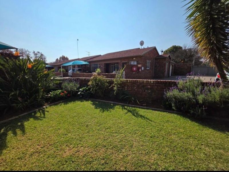 Front view of a face brick apartment complex featuring a well-maintained lawn, landscaped garden, and secure boundary wall.