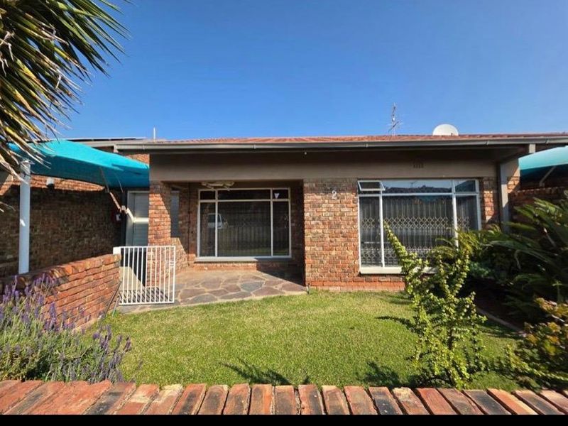 Front elevation of a face brick apartment featuring a paved patio area, secure window grilles, and a well-maintained front garden.