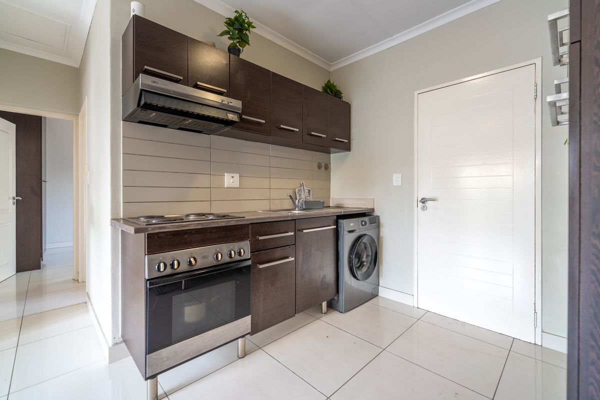 Compact kitchen featuring dark wood cabinetry, built-in oven and hob, extractor fan, and tiled flooring with a neutral finish.