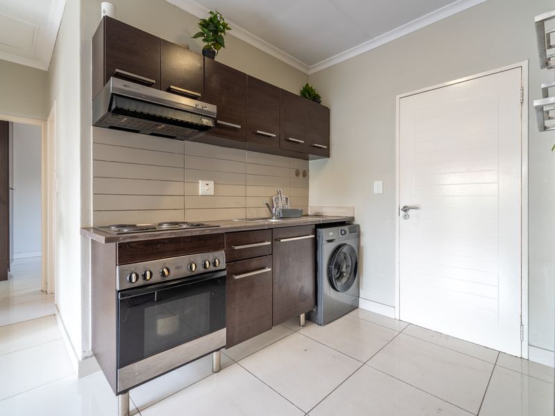 Compact kitchen featuring dark wood cabinetry, built-in oven and hob, extractor fan, and tiled flooring with a neutral finish.