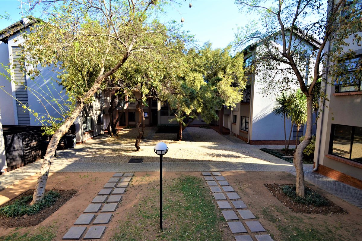 A view of the apartment complex's rear courtyard featuring paved walkways, gravel landscaping, and mature trees between the building wings.
