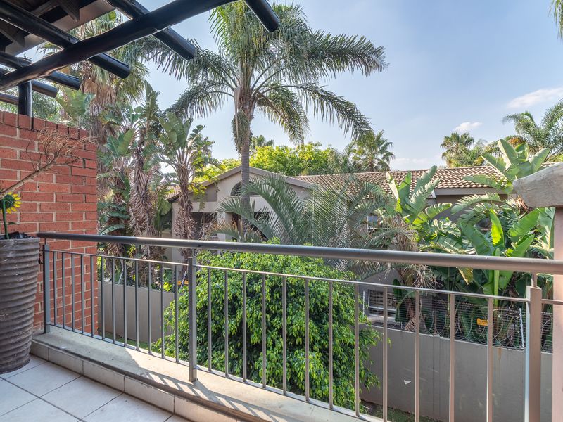 A private balcony featuring tiled flooring, a metal safety railing, and an exposed brick wall, overlooking a lush garden area.