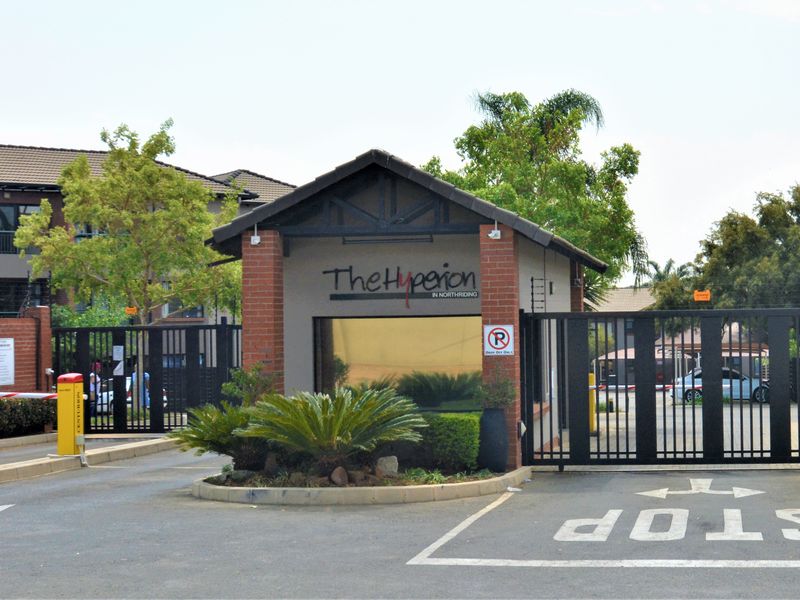 The secure entrance to The Hyperion complex, featuring a gated access point, boom gate, and brick-accented guardhouse structure.