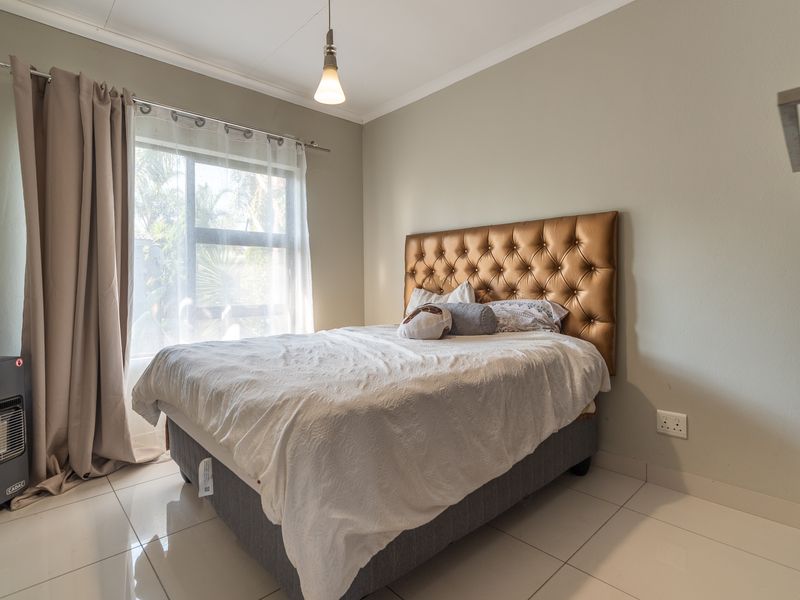 A well-maintained bedroom featuring neutral wall tones, tiled flooring, and a large window allowing for natural light.