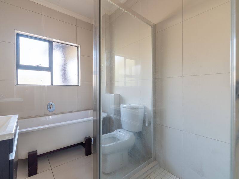 A functional bathroom featuring a bathtub, a separate shower enclosure with glass door, a toilet, and a vanity unit with tiled finishes throughout.