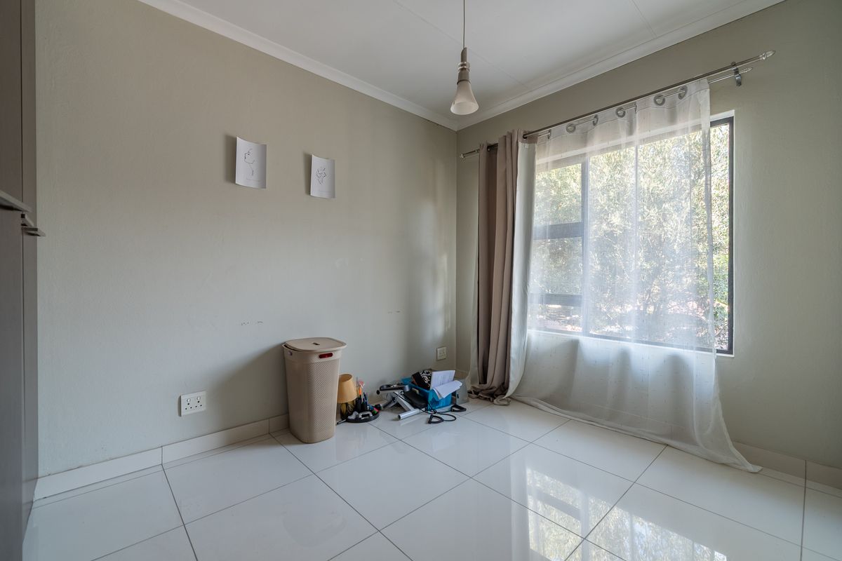 A bright, empty bedroom featuring white tiled flooring, neutral wall tones, and a large window with natural light.