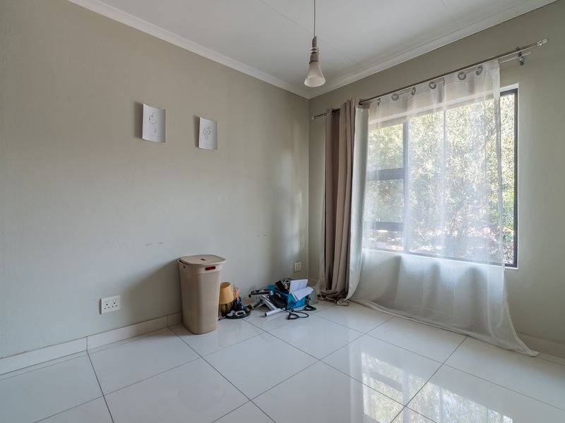 A bright, empty bedroom featuring white tiled flooring, neutral wall tones, and a large window with natural light.