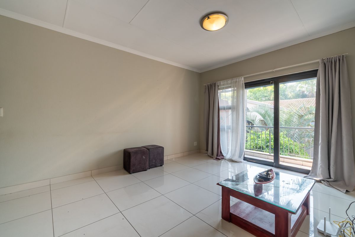 A bright, empty living room featuring large format floor tiles and a sliding glass door leading to a balcony.