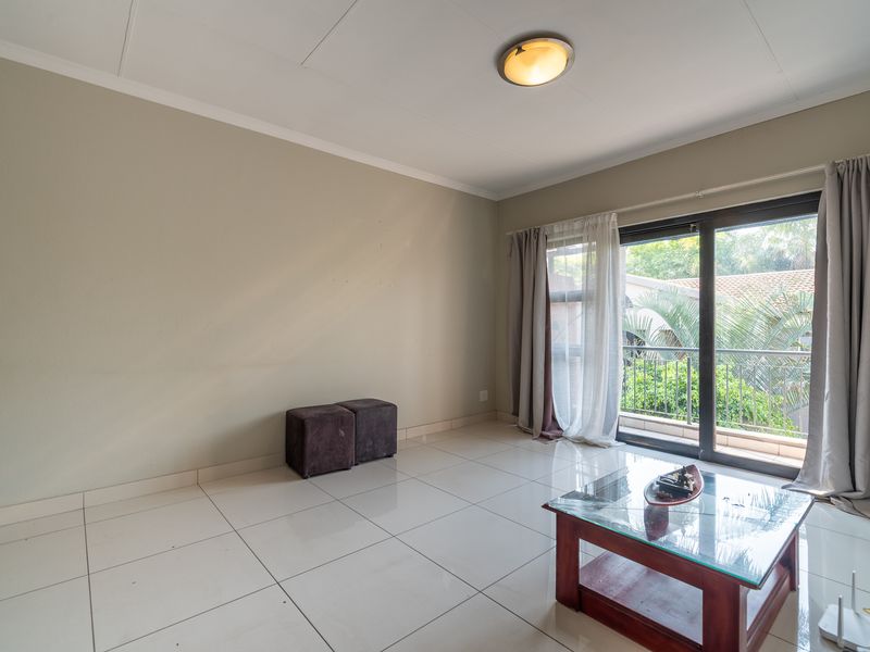 A bright, empty living room featuring large format floor tiles and a sliding glass door leading to a balcony.