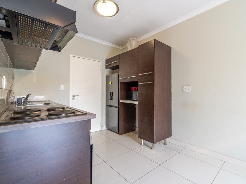 A functional kitchen featuring dark wood-finish cabinetry, tiled flooring, an integrated hob with extractor fan, and ample storage space.