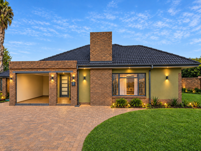 A well-maintained single-story brick home featuring a paved driveway, integrated garage, and manicured front garden with modern exterior lighting.