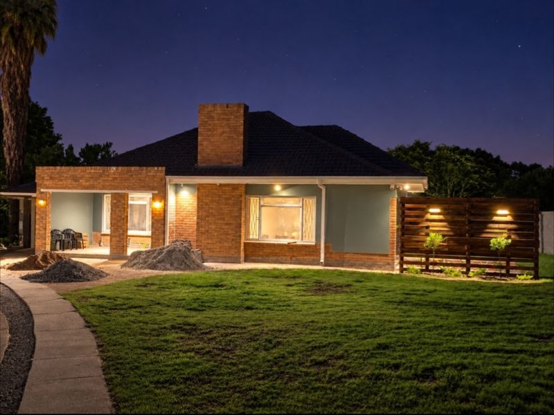 Rear view of a brick and rendered house at night, featuring a covered patio, timber privacy screen, and an established lawn area.