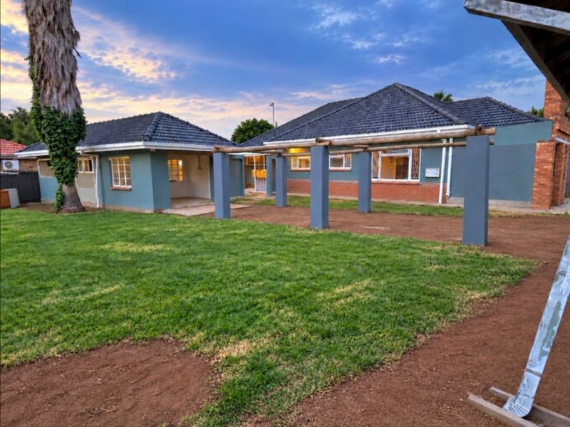 Rear view of the property featuring a tiled roof, a pergola structure, and a spacious garden area with established lawn.