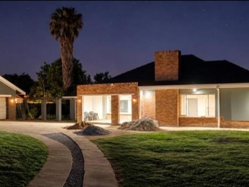 Night view of a residential property featuring a brick facade, double garage, paved driveway, and landscaped garden with exterior lighting.