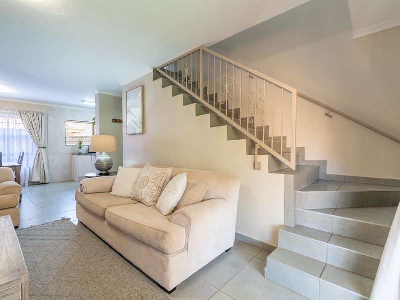 Open plan living area featuring tiled flooring and a staircase with a decorative metal balustrade, leading towards a kitchen space.