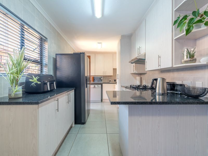 A functional kitchen featuring light wood-grain cabinetry, dark granite countertops, a gas hob with extractor fan, and neutral tiled flooring.