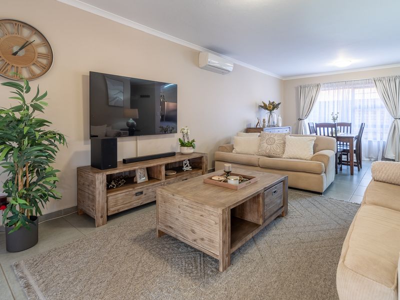 A well-maintained open-plan living and dining area featuring tiled flooring, neutral wall tones, and a wall-mounted split-system air conditioner.