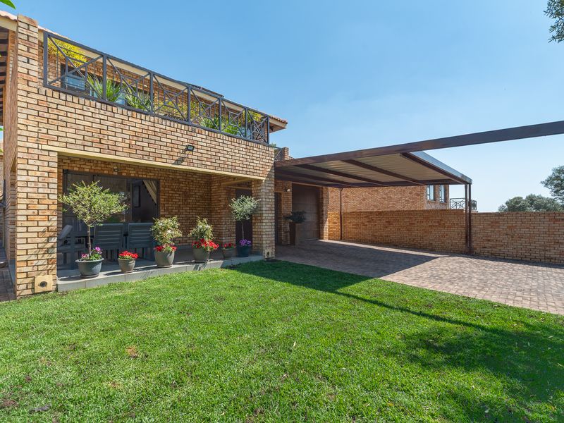 Rear view of a face brick townhouse featuring a covered patio, upper balcony, paved carport, and a well-maintained garden lawn.