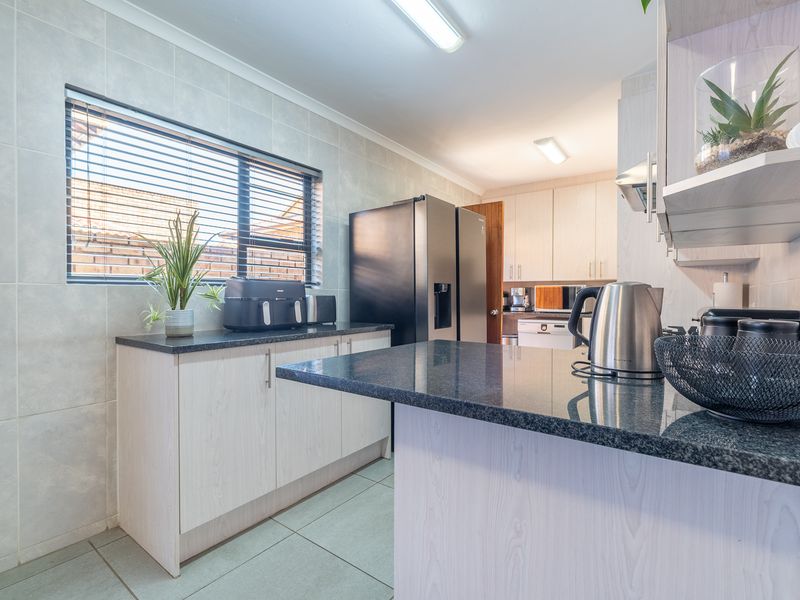 A functional kitchen featuring granite countertops, light-toned cabinetry, tiled walls, and tiled flooring with ample natural light from the window.