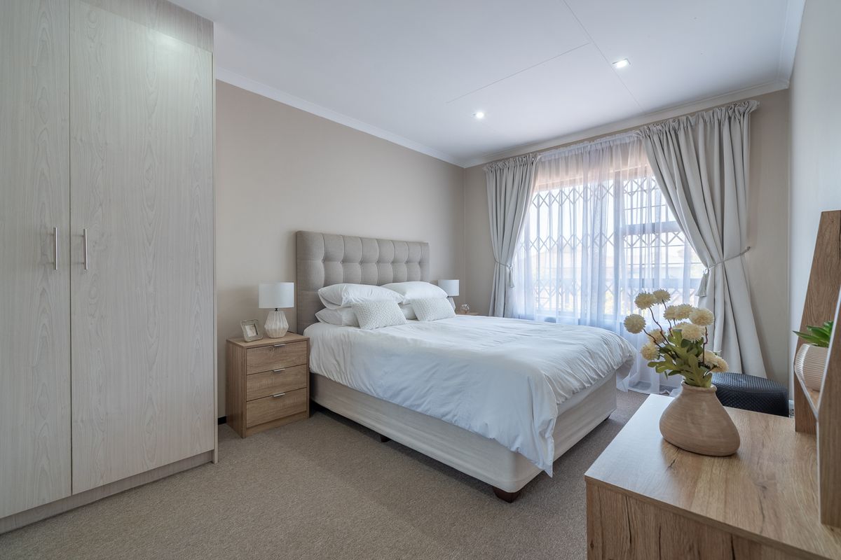 A well-maintained bedroom featuring neutral tones, carpet flooring, recessed lighting, and a large built-in wardrobe with light wood-grain finish.
