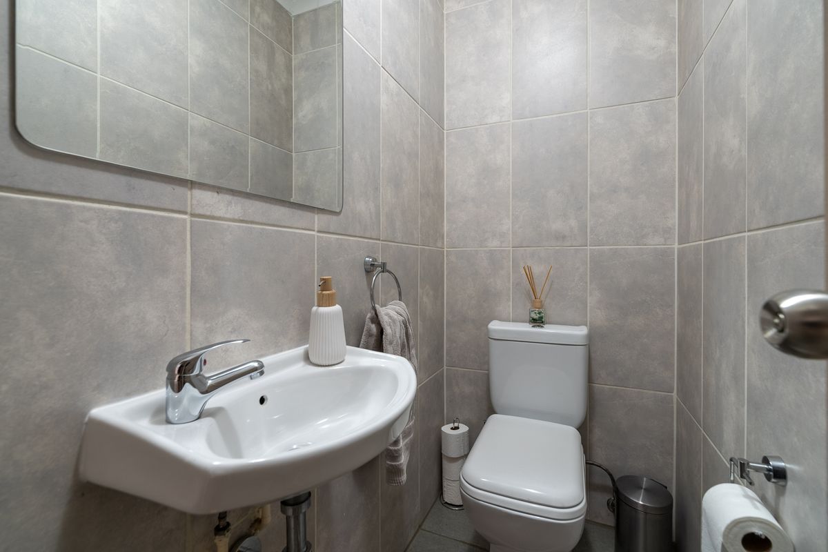 A compact, modern guest bathroom featuring neutral grey wall tiles, a wall-mounted basin with chrome fixtures, and a standard toilet.