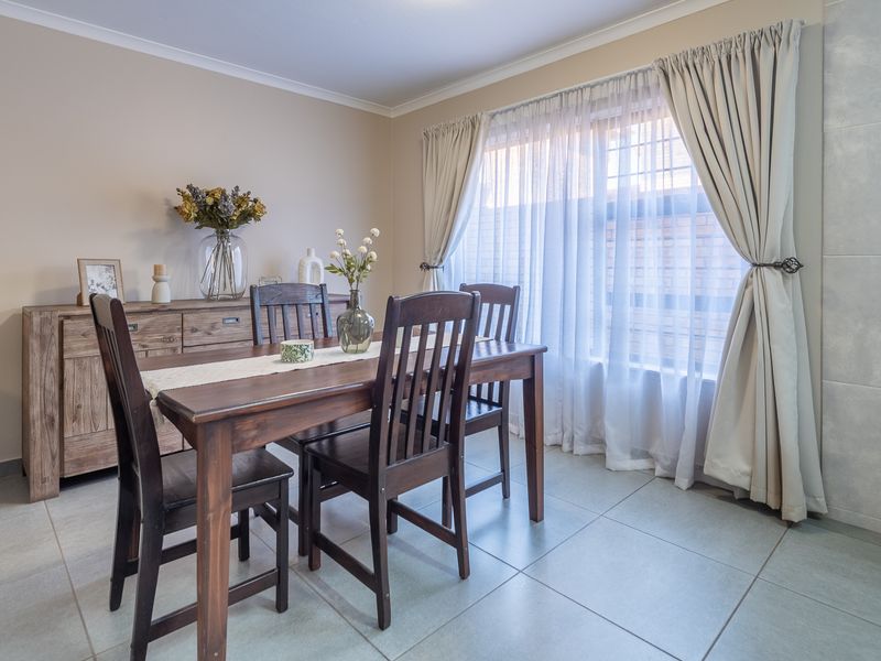A well-maintained dining room featuring neutral wall tones, tiled flooring, and large windows with elegant curtain treatments, providing a bright and inviting atmosphere.