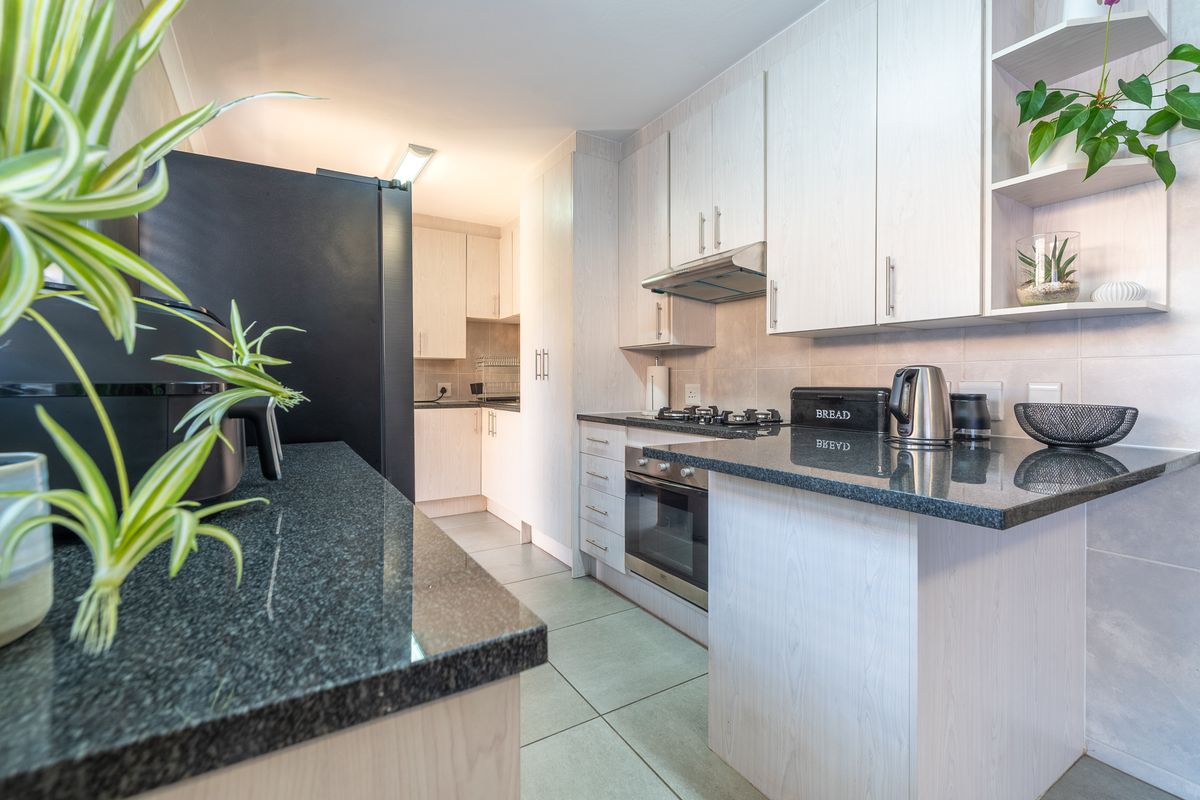 A functional kitchen featuring light-toned cabinetry, dark granite countertops, a built-in oven with gas hob, and tiled flooring.