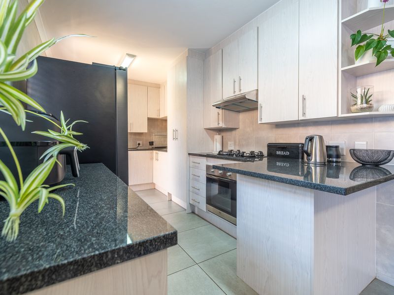 A functional kitchen featuring light-toned cabinetry, dark granite countertops, a built-in oven with gas hob, and tiled flooring.
