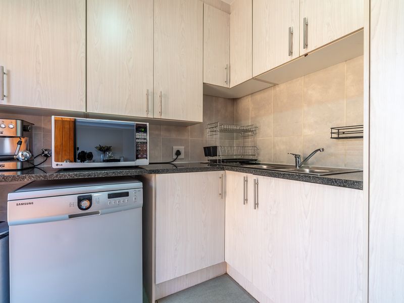 Compact kitchen featuring light wood-grain laminate cabinetry, granite countertops, a stainless steel sink, and tiled backsplash.