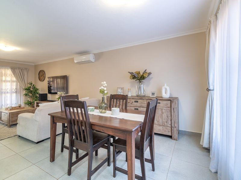 Spacious open-plan living and dining area featuring neutral tiled flooring and a wall-mounted air conditioning unit, with access to natural light.